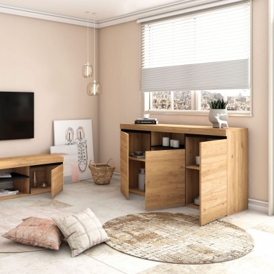 Móvel de madeira clara com portas abertas, tapete redondo bege e almofadas no chão numa sala clara com cortinas brancas e quadro encostado.