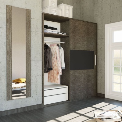 Armário de madeira escura com portas de correr, prateleiras com roupas e gavetas brancas ao lado de espelho vertical numa parede cinzenta.