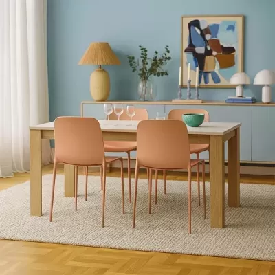 Mesa de madeira clara com tampo branco e quatro cadeiras cor de salmão numa sala azul com tapete bege e decoração