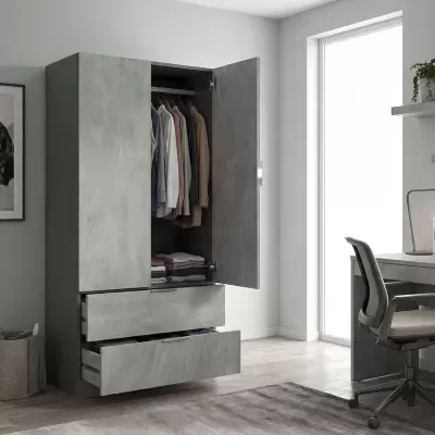 Roupeiro cinza com portas abertas e gavetas, roupa pendurada e dobrada dentro, ao lado de cadeira de escritório e tapete cinzento