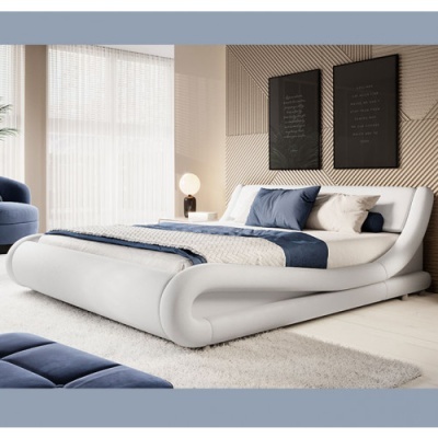 Cama branca curvada com roupa de cama azul e bege, almofadas, tapete branco e duas molduras pretas na parede
