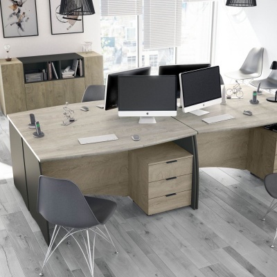 Mesas de escritório com tampos de madeira clara, cadeiras cinza e computadores em ambiente claro