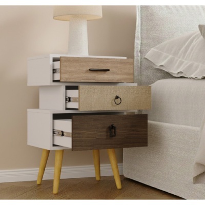 Mesa de cabeceira de madeira com três gavetas coloridas e lâmpada em cima ao lado de cama.