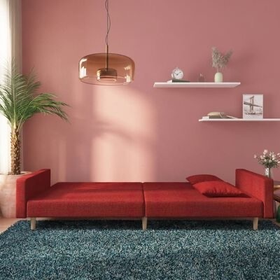 Sofá modular vermelho com almofada em sala decorada com tapete azul, prateleiras brancas, planta e luminária âmbar