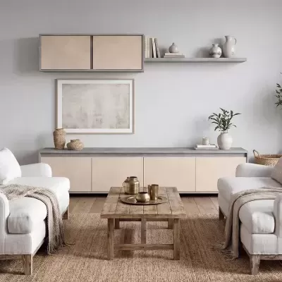Sala de estar com poltronas brancas, mesa de centro em madeira, móvel baixo bege, prateleira cinza com livros e vasos, quadro abstrato, tapete de fibra natural e chão em madeira clara.