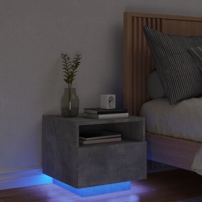 Mesa de cabeceira cinzenta com iluminação LED azul na base ao lado de cama com roupa cinzenta