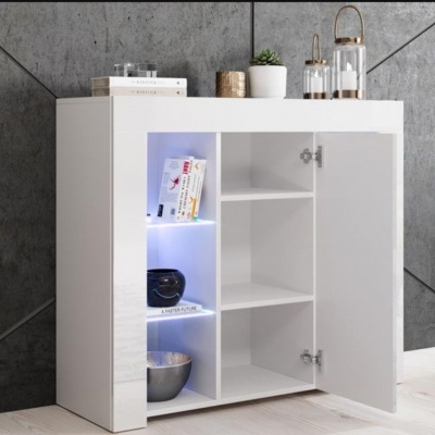 Móvel branco com prateleiras iluminadas e porta aberta com livros e utensílios