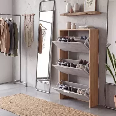 Móvel organizador de sapatos em madeira clara com três compartimentos inclinados cinza junto a espelho de corpo inteiro e tapete bege em ambiente minimalista
