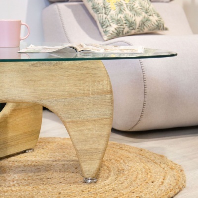 Mesa de centro com tampo de vidro e base de madeira clara sobre tapete redondo de fibras naturais