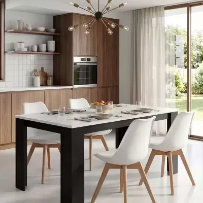 Mesa de jantar branca com cadeiras brancas e pernas em madeira clara numa cozinha moderna com armários em madeira e janela grande