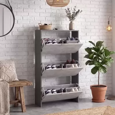 Sapateira cinza com sapatos, banco de madeira, planta em vaso e candeeiro suspenso numa sala com parede branca de tijolo.