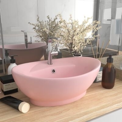 Lavabo oval rosa com torneira numa bancada de madeira clara com decoração e espelho ao fundo