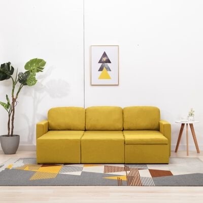 Sofá amarelo moderno numa sala com tapete colorido, planta, mesa lateral e quadro de triângulos na parede branca