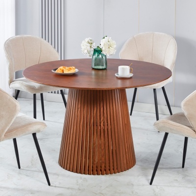 Mesa de jantar redonda em madeira com base torneada, quatro cadeiras estofadas bege e objetos em cima da mesa