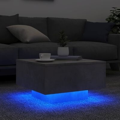 Mesa de centro cinzenta com luz azul na base ao lado de sofá cinzento com almofadas.