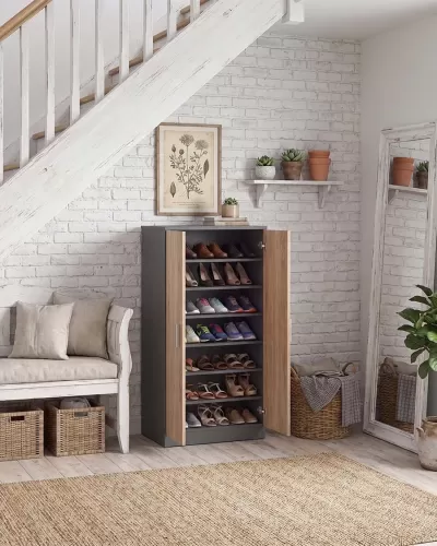 Armário sapateira com portas castanho claro e estrutura cinza escuro, cheio de sapatos, em ambiente com parede de tijolo branco e piso de madeira clara