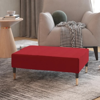 Pufe retangular vermelho com pés de madeira e metal num ambiente de sala com poltrona e mesa