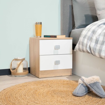 Mesa de cabeceira de madeira clara com gavetas brancas ao lado de cama com edredão xadrez cinza e branco, tapete redondo de fibras e chinelos cinza felpudos