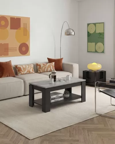 Sala de estar com mesa de centro retangular cinza e preta, sofá bege com almofadas castanhas, candeeiro de pé prateado e lâmpada amarela em mesa preta