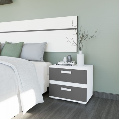 Mesa de cabeceira branca e cinzenta com gavetas, vaso branco e livros ao lado de cama com almofadas verdes e cinzentas