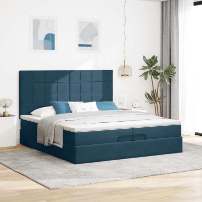Cama de casal azul escuro estofada com cabeceira, roupa de cama branca e cinza, almofadas, tapete cinzento, mesa de cabeceira branca, candeeiro transparente, quadros e planta junto a janela.