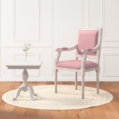 cadeira estofada rosa com mesa pequena branca sobre tapete redondo bege num interior com parede branca