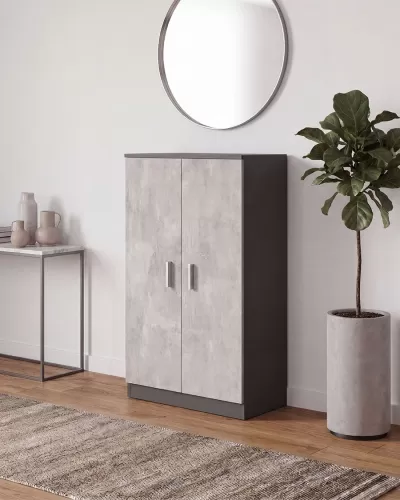 Armário de madeira cinzento de duas portas junto à parede com espelho redondo, mesa com jarros e vaso alto com planta verde