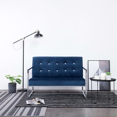 Sofá azul escuro com candeeiro, plantas, tapete listrado e mesa lateral preta numa sala minimalista