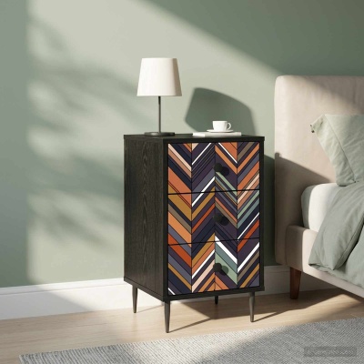 Mesa de cabeceira em madeira escura com gavetas decoradas em padrão geométrico multicolorido, candeeiro branco e chávena em cima