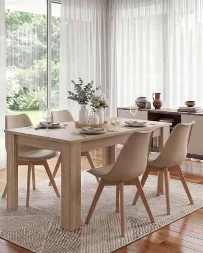 Mesa de jantar em madeira clara com cadeiras bege e decoração com flores em sala iluminada