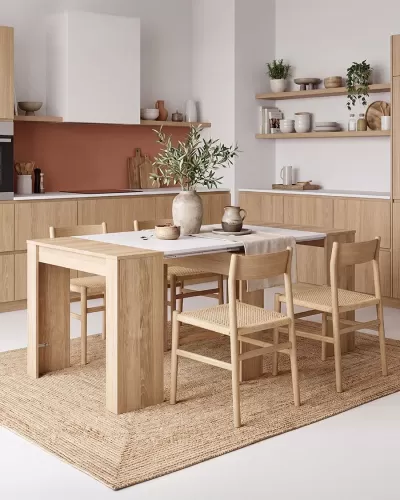 Mesa de jantar extensível de madeira clara com cadeiras de madeira e assentos em fibra natural num ambiente de cozinha moderna.