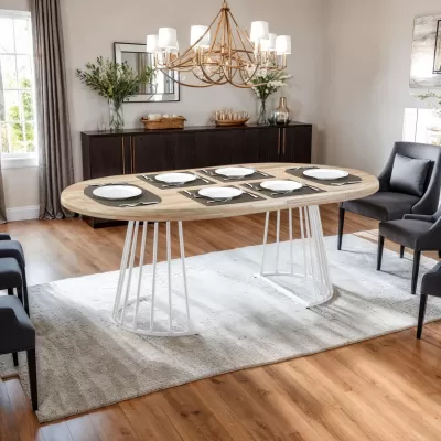 Mesa de jantar oval de madeira clara com pernas metálicas brancas, cadeiras cinzentas e candeeiro dourado numa sala com aparador escuro e decoração moderna