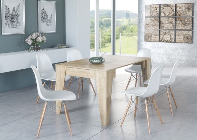 Mesa de jantar de madeira clara com seis cadeiras brancas em sala decorada, chão cinzento, quadros e janela grande com vista verde