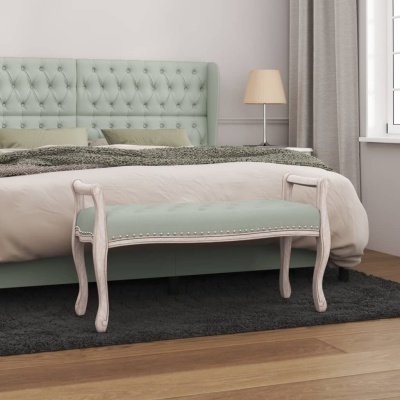 Banco estofado verde água junto a cama com cabeceira verde e colcha creme em quarto com cortinas cinza