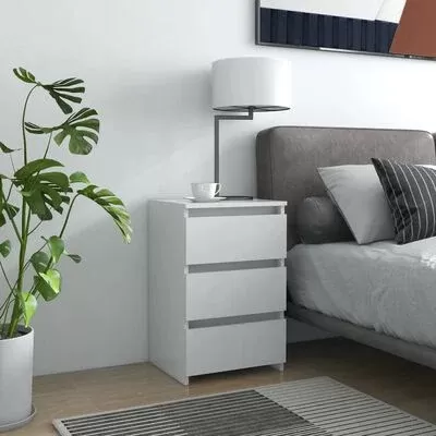 Móvel branco com três gavetas, candeeiro e chávena, cama cinza com almofadas, planta e tapete