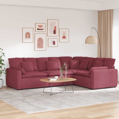 sofá de canto vermelho vinho num sala com mesa de centro oval e quadros decorativos