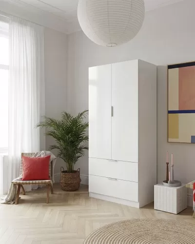 Armário branco de madeira com duas portas e gavetas numa sala, cadeira com almofada vermelha e planta em vaso ao lado