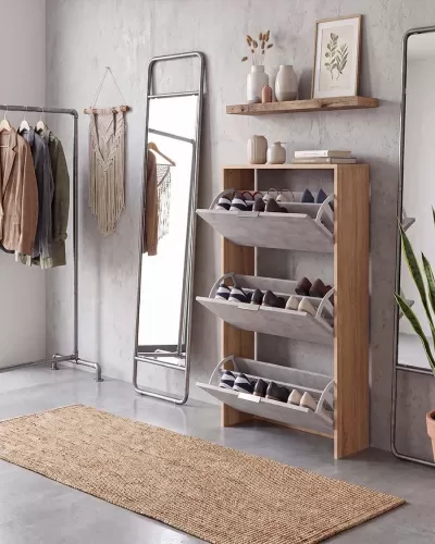 Móvel organizador de sapatos em madeira clara com três compartimentos inclinados cinza junto a espelho de corpo inteiro e tapete bege em ambiente minimalista