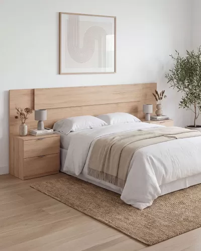 Quarto com cama de madeira clara, roupa de cama branca e manta bege, 2 mesinhas de cabeceira com candeeiros e vasos, e planta verde no canto