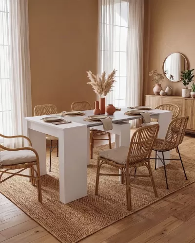Mesa de jantar branca com cadeiras de rattan e decoração em ambiente luminoso