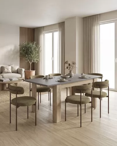 Mesa de jantar com tampo cinzento e cadeiras verdes num ambiente minimalista com cortinas bege e planta em vaso de barro