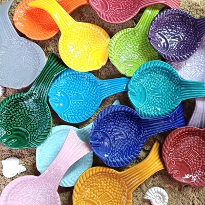 Pequenas travessas em formato de peixe coloridas sobre areia com conchas brancas
