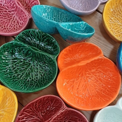 Pratos pequenos de cerâmica texturizados em formato de folhas, multicoloridos, sobre mesa de madeira.