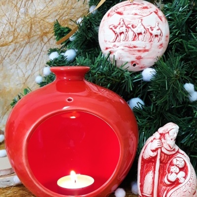 Castiçal cerâmico vermelho com vela, ornamento e figura cerâmica vermelha e branca junto a árvore de Natal