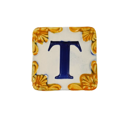 Azulejo cerâmico quadrado com letra T azul e ornamentos amarelos nos cantos