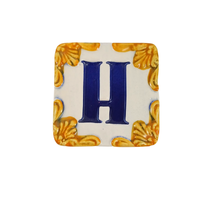 Azulejo cerâmico quadrado com letra H azul e ornamentos amarelos nos cantos