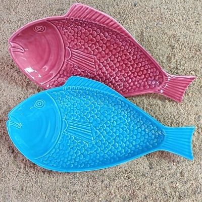 Dois pratos em cerâmica vermelha e azul em forma de peixes sobre areia
