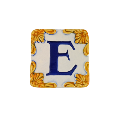 Azulejo cerâmico com letra E azul e decoração amarela nos cantos