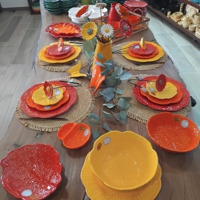 Conjunto de loiça colorida em cerâmica com pratos e tigelas amarelas, laranja e vermelhas numa mesa de madeira com decoração floral.