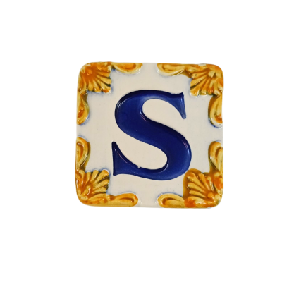 Azulejo cerâmico branco com letra S azul e ornamentos amarelos nos cantos